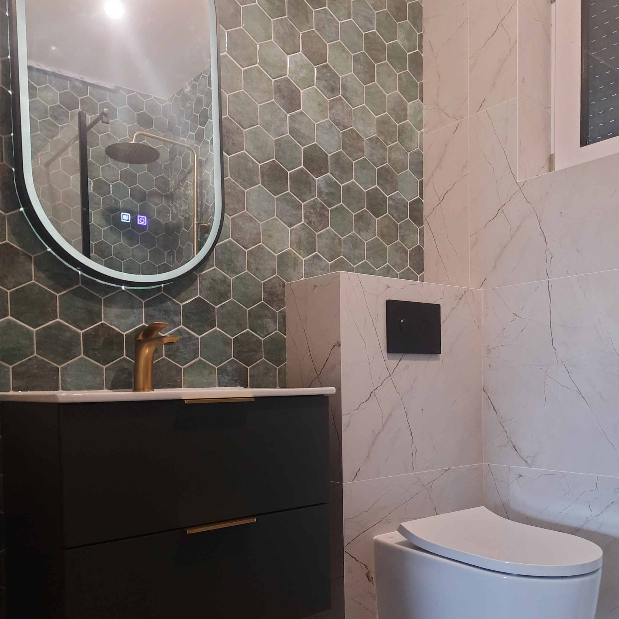 Nowoczesna łazienka z umywalką nablatową, złotą armaturą i lustrem LED, wykończona heksagonalnymi płytkami w odcieniach zieleni oraz marmurowymi płytkami.