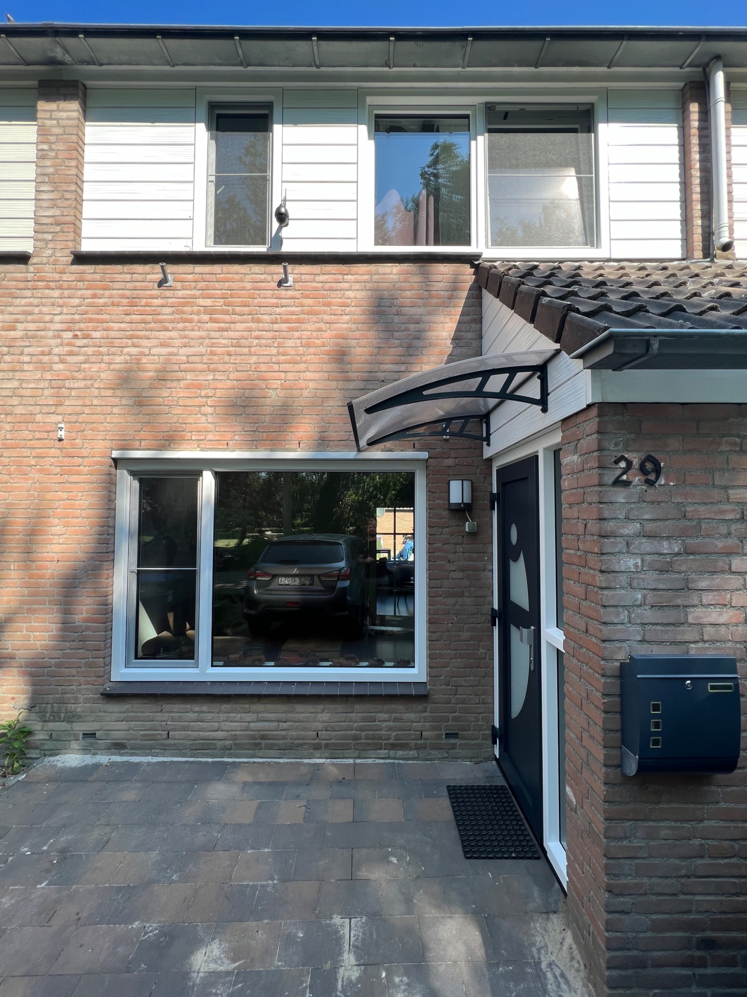 Fasada dwukondygnacyjnego domu z cegły z nową stolarką okienną i zadaszeniem nad wejściem, widoczny numer domu 29 i skrzynka pocztowa.