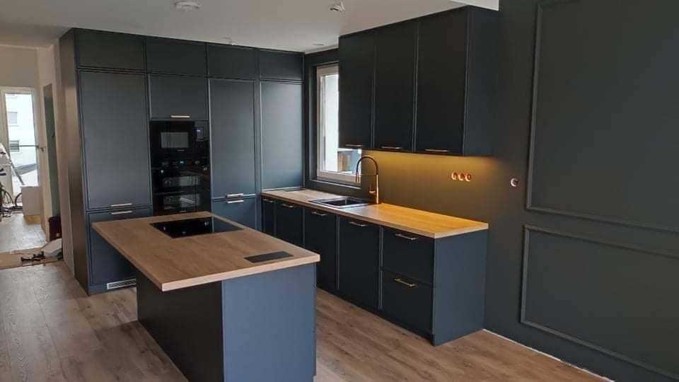 Nowoczesna kuchnia z ciemnymi, grafitowymi szafkami i drewnianym blatem, oświetlenie podszafkowe, wyspa kuchenna z płytą indukcyjną, minimalistyczny design.