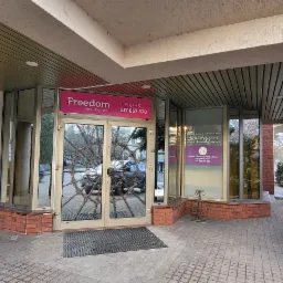 Wejście do biura nieruchomości Freedom z dekoracyjnymi, metalowymi zdobieniami na szklanych drzwiach, widoczny szyld z numerem telefonu i logo firmy.