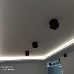 Nowoczesny biały sufit z podświetleniem LED wzdłuż krawędzi i czarnymi, minimalistycznymi reflektorami punktowymi.