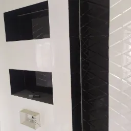 Biało-czarna ściana w łazience z wnękami i dekoracyjnymi płytkami. Widoczny fragment instalacji elektrycznej.
