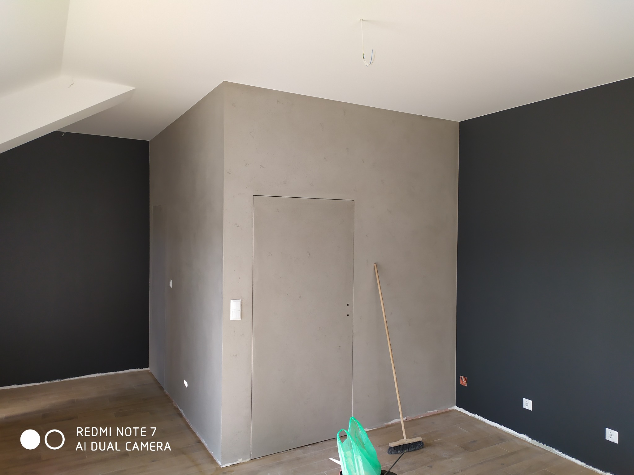 Wnętrze pokoju po remoncie, ściany pomalowane na ciemny grafit i wykończone gładzią w odcieniach szarości, widoczne listwy przypodłogowe, drewniana podłoga i narzędzia pracy.