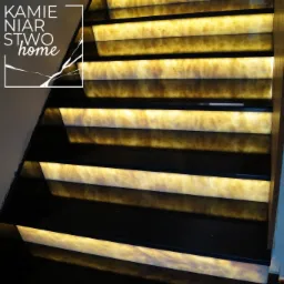 Schody wewnętrzne z podświetlanymi stopniami z onyksu Sugar i stopniami z czarnego granitu, widoczne logo firmy w lewym g&oacute;rnym rogu.