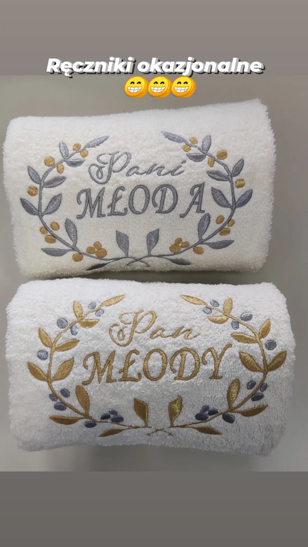 Dwa białe, złożone ręczniki frotte z okolicznościowym haftem: 'Pani Młoda' w szarym odcieniu i 'Pan Młody' w złotym odcieniu, oba otoczone haftowanymi gałązkami z listkami i owocami.
