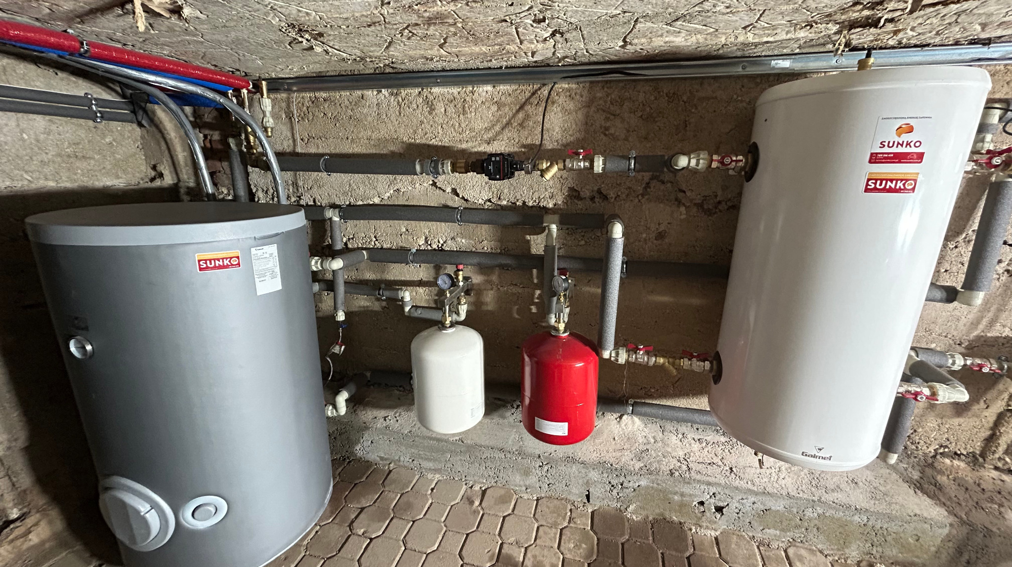 Dwa zbiorniki buforowe Sunko i Galmet w kotłowni w Białymstoku, z widoczną instalacją hydrauliczną i manometrami na tle surowej ściany.