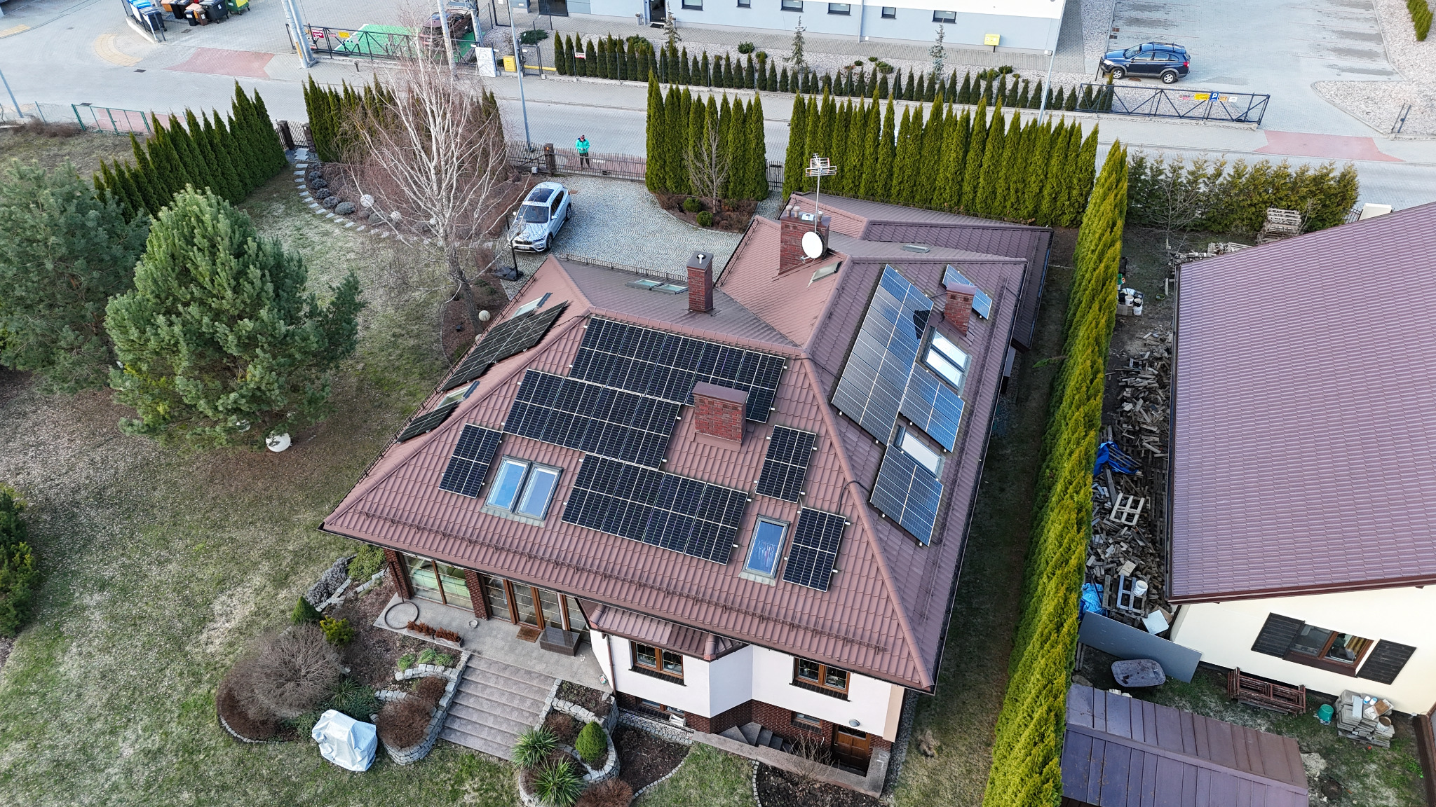 Widok z drona na dom jednorodzinny w Białymstoku z zainstalowanymi panelami słonecznymi na dachu pokrytym brązową dachówką, widoczny ogród i podjazd.