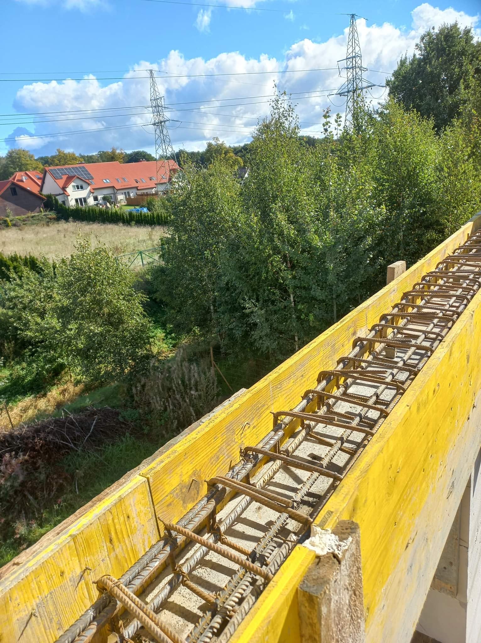 Żółte szalunki zbrojeniowe na budowie w Cewicach, w tle domy jednorodzinne i słupy wysokiego napięcia.