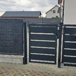 Nowoczesne, antracytowe ogrodzenie panelowe z przesłoną i brama wjazdowa z poziomymi profilami, widok z poziomu chodnika przed posesją.
