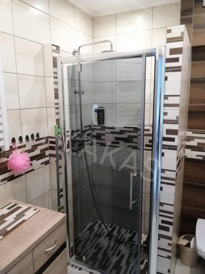 Nowoczesna kabina prysznicowa z chromowanymi profilami i deszczownicą, w łazience wykończonej płytkami w odcieniach beżu i brązu, z dekoracyjnym pasem mozaiki.