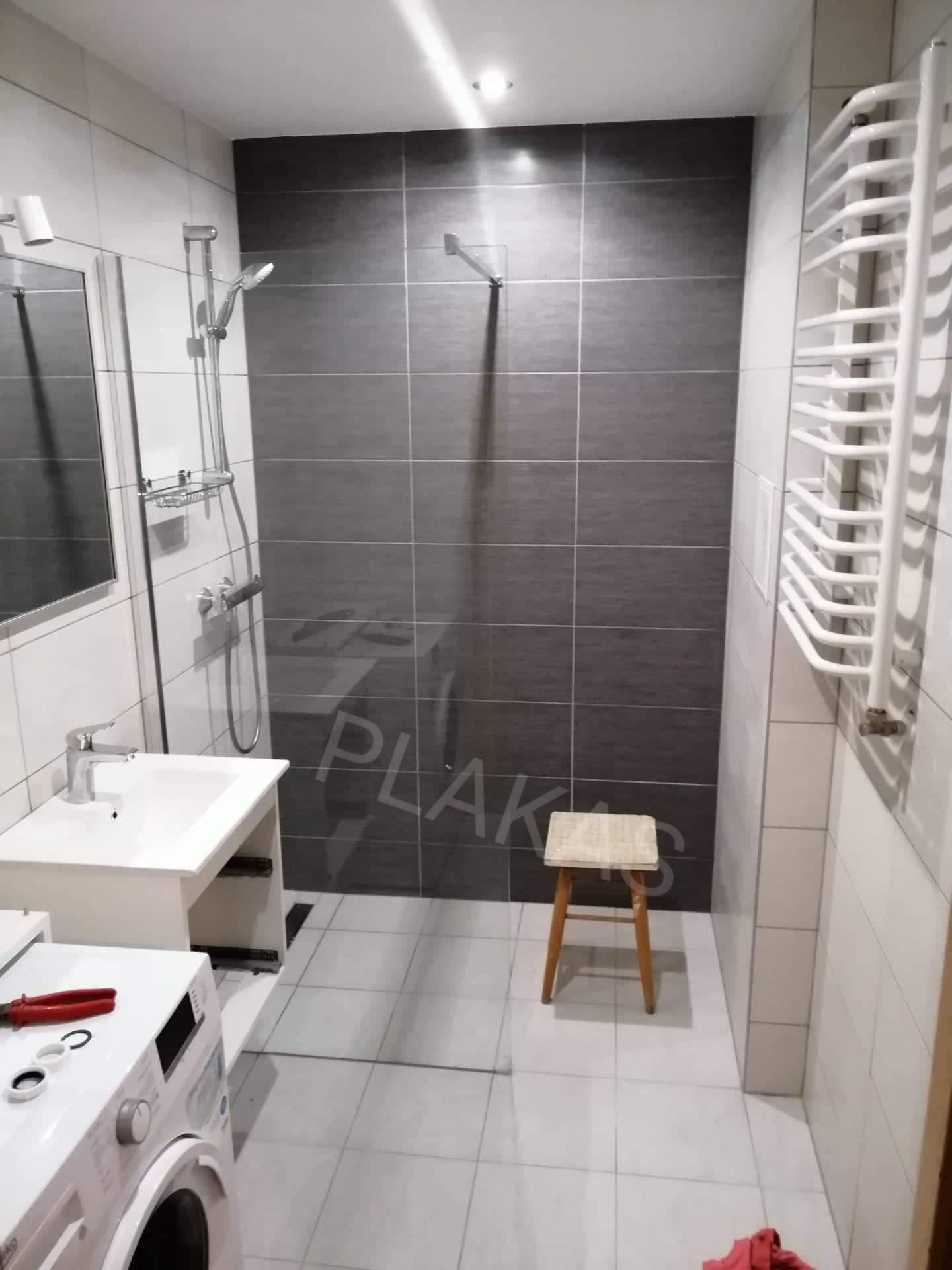 Wykończona łazienka w Wilczkowie z szarymi płytkami pod prysznicem, białą umywalką, grzejnikiem drabinkowym i pralką z widocznymi narzędziami.