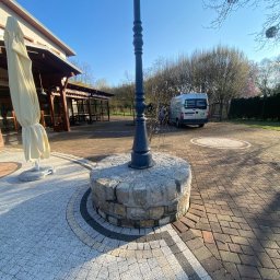 ABC Mycie Wrocław - Ułożona z kostki brukowej powierzchnia placu z ozdobnymi wzorami, w tle budynek z zadaszeniem i zaparkowany bus z widocznym logo firmy.