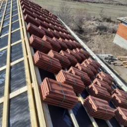 Przygotowanie do ułożenia dachówek ceramicznych na nowej konstrukcji więźby dachowej pokrytej membraną, widok z góry na rozległy krajobraz.