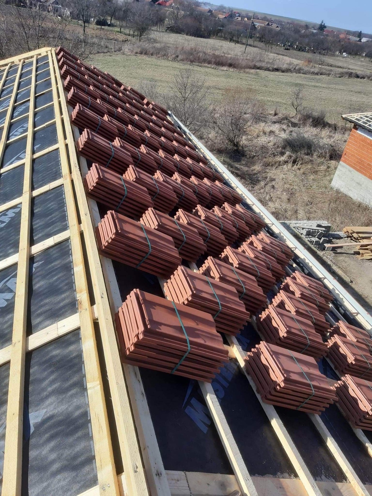 Przygotowanie do ułożenia dachówek ceramicznych na nowej konstrukcji więźby dachowej pokrytej membraną, widok z góry na rozległy krajobraz.