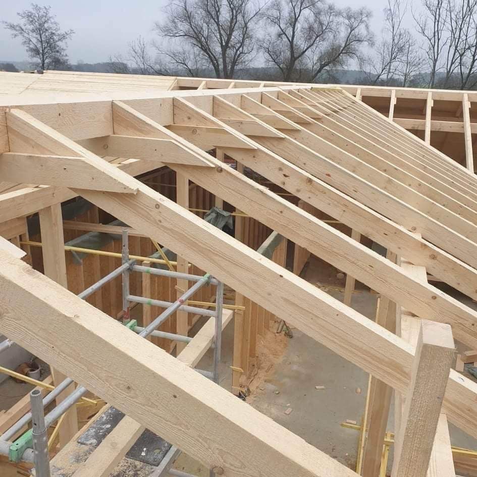 Konstrukcja drewniana dachu w trakcie montażu, widoczne krokwie i rusztowanie, surowy stan, pochmurne niebo w tle.