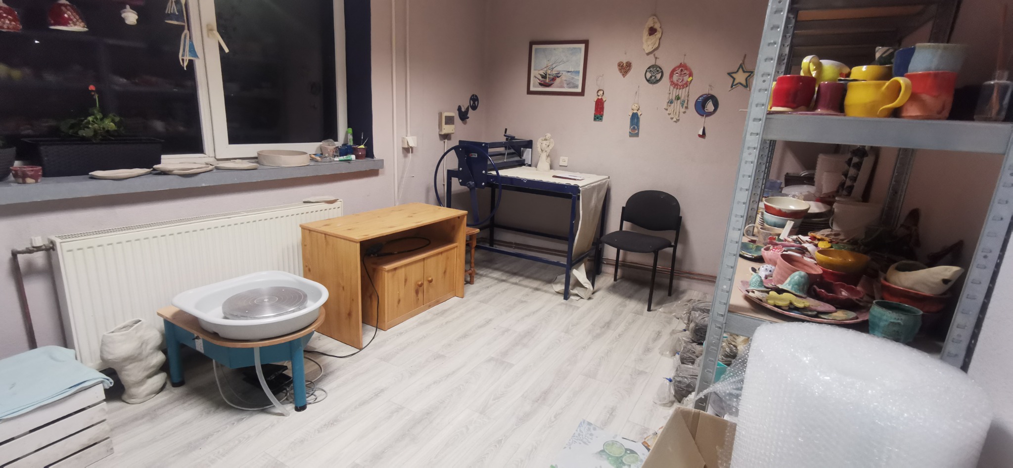Pracownia garncarska z kołem garncarskim, prasą do gliny, półkami pełnymi naczyń i dekoracjami ściennymi.