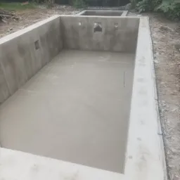 Wylany beton wewnątrz betonowych ścian fundamentowych z otworami na instalacje, widok z góry na budowie w ogrodzie.