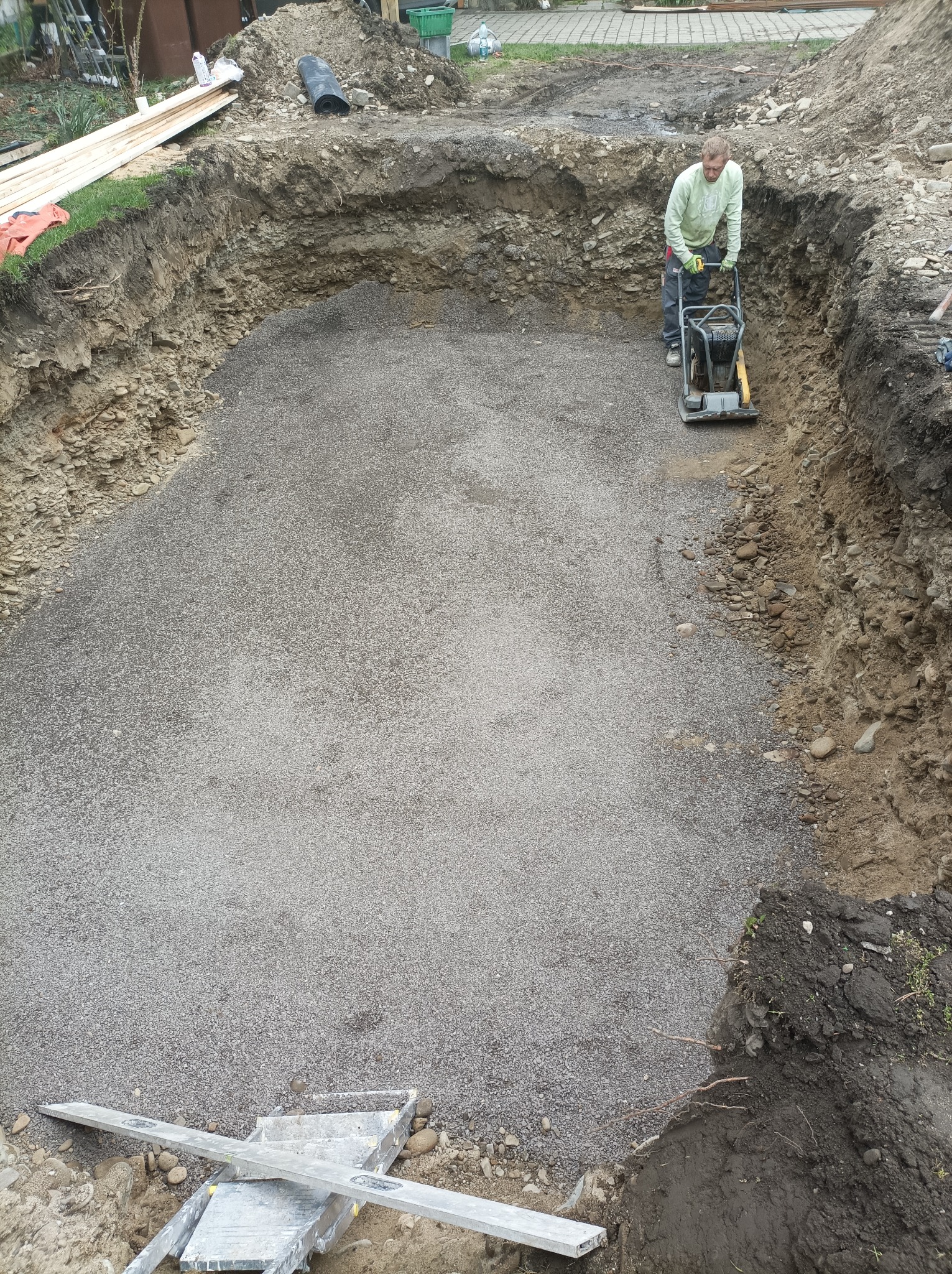 Pracownik zagęszcza podłoże z kruszywa w wykopie pod fundamenty za pomocą zagęszczarki wibracyjnej.