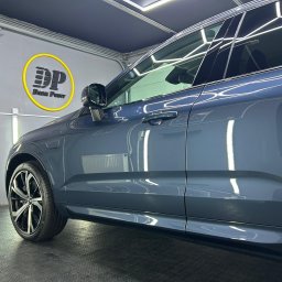 DarkPoint DANIEL KNYS - Błyszczący, szary samochód SUV z przyciemnionymi szybami, zaparkowany w dobrze oświetlonym garażu z logo firmy detailerskiej na ścianie.