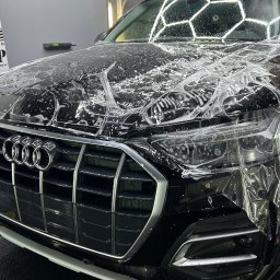 DarkPoint DANIEL KNYS - Czarny samochód Audi z nałożoną folią ochronną na przedniej masce i reflektorach, widoczne logo firmy Dark Point w tle.