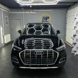 Błyszczący, czarny samochód Audi z widocznym logo firmy detailingowej Dark Point, zaparkowany w dobrze oświetlonym garażu z podłogą z tworzywa sztucznego.