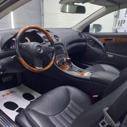 DarkPoint DANIEL KNYS - Wnętrze luksusowego samochodu Mercedes SL z drewnianą kierownicą i czarną skórzaną tapicerką po zabiegach pielęgnacyjnych, widoczna mata ochronna na podłodze z logo ADBL oraz logo DarkPoint...