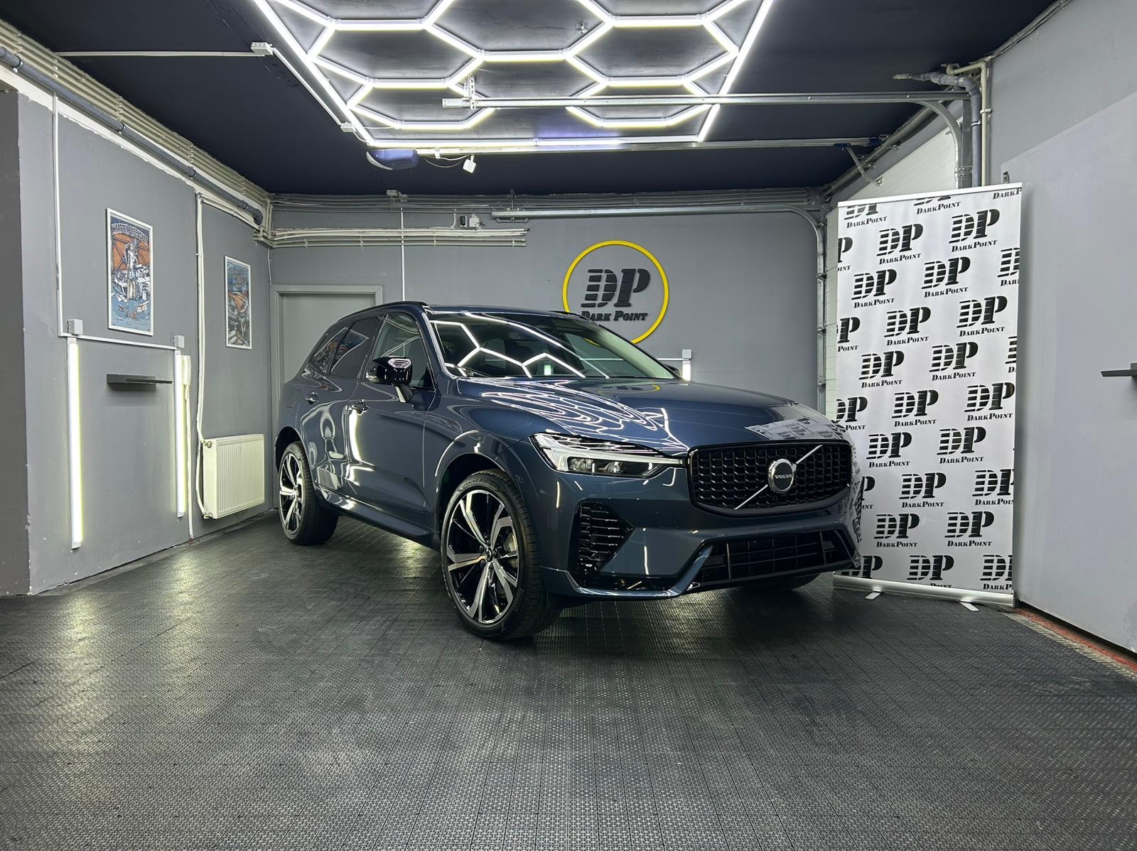 Błękitny SUV Volvo po zabiegach pielęgnacyjnych w studiu detailingu w Konstantynowie Łódzkim, widoczne logo firmy na ścianie i baner reklamowy.