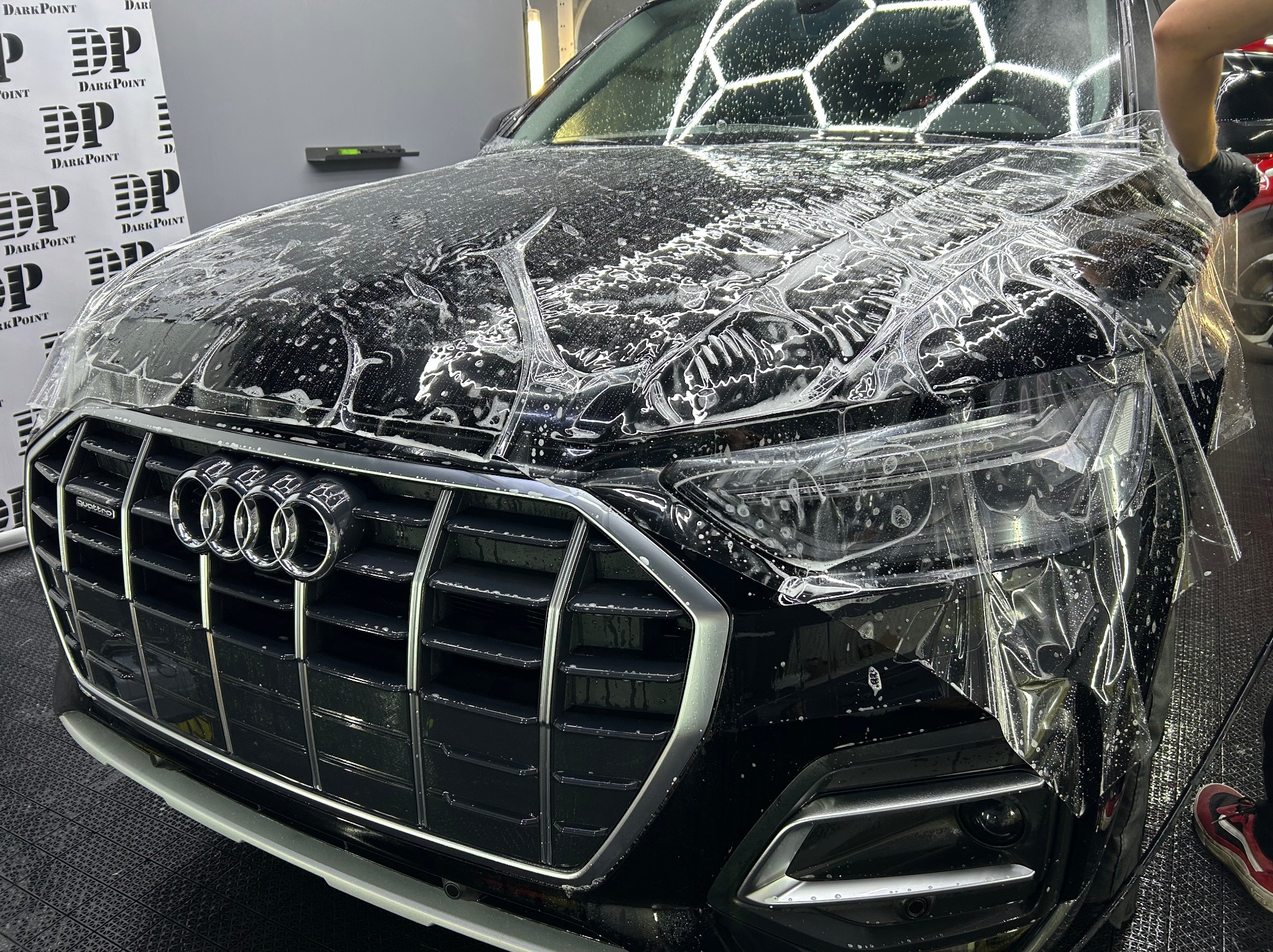 Czarny samochód Audi z nałożoną folią ochronną na przedniej masce i reflektorach, widoczne logo firmy Dark Point w tle.