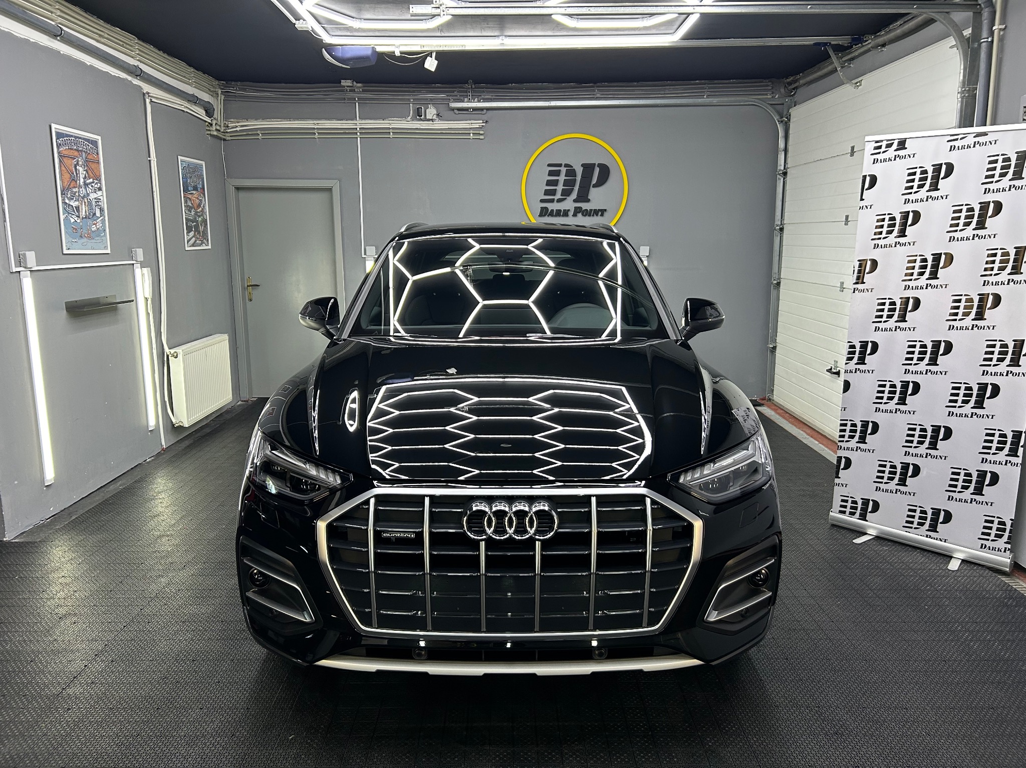 Błyszczący, czarny samochód Audi z widocznym logo firmy detailingowej Dark Point, zaparkowany w dobrze oświetlonym garażu z podłogą z tworzywa sztucznego.