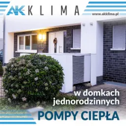 Biała pompa ciepła zainstalowana przed nowoczesnym domem jednorodzinnym z ciemnej cegły, widoczna zza kwitnącego krzewu ozdobnego, logo firmy w górnej części zdjęcia.