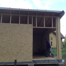 P.H.U. GRONEK ARKADIUSZ GRONKOWSKI - Konstrukcja szkieletowa budynku w trakcie budowy z częściowo zamontowaną płytą OSB, widoczny pracownik wewnątrz.