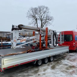 P.H.U. GRONEK ARKADIUSZ GRONKOWSKI - Przyczepa z podnośnikiem teleskopowym EasyLift na tle zimowego krajobrazu i czerwonego busa firmy Artech-Okna.pl.