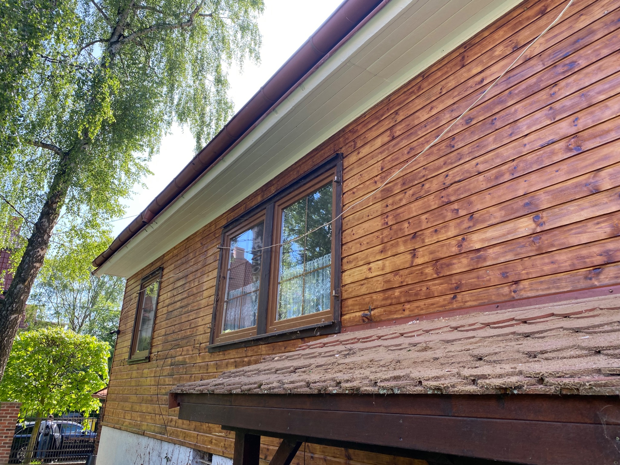 Świeżo pomalowana drewniana elewacja domu z widocznymi oknami i fragmentem dachu, z delikatnym połyskiem farby w słonecznym świetle.