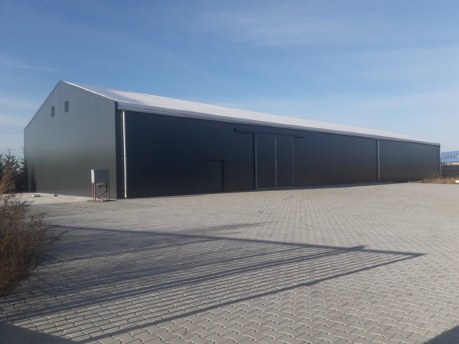 Gotowa hala magazynowa z czarnymi ścianami i białym dachem, widok z zewnątrz w słoneczny dzień.
