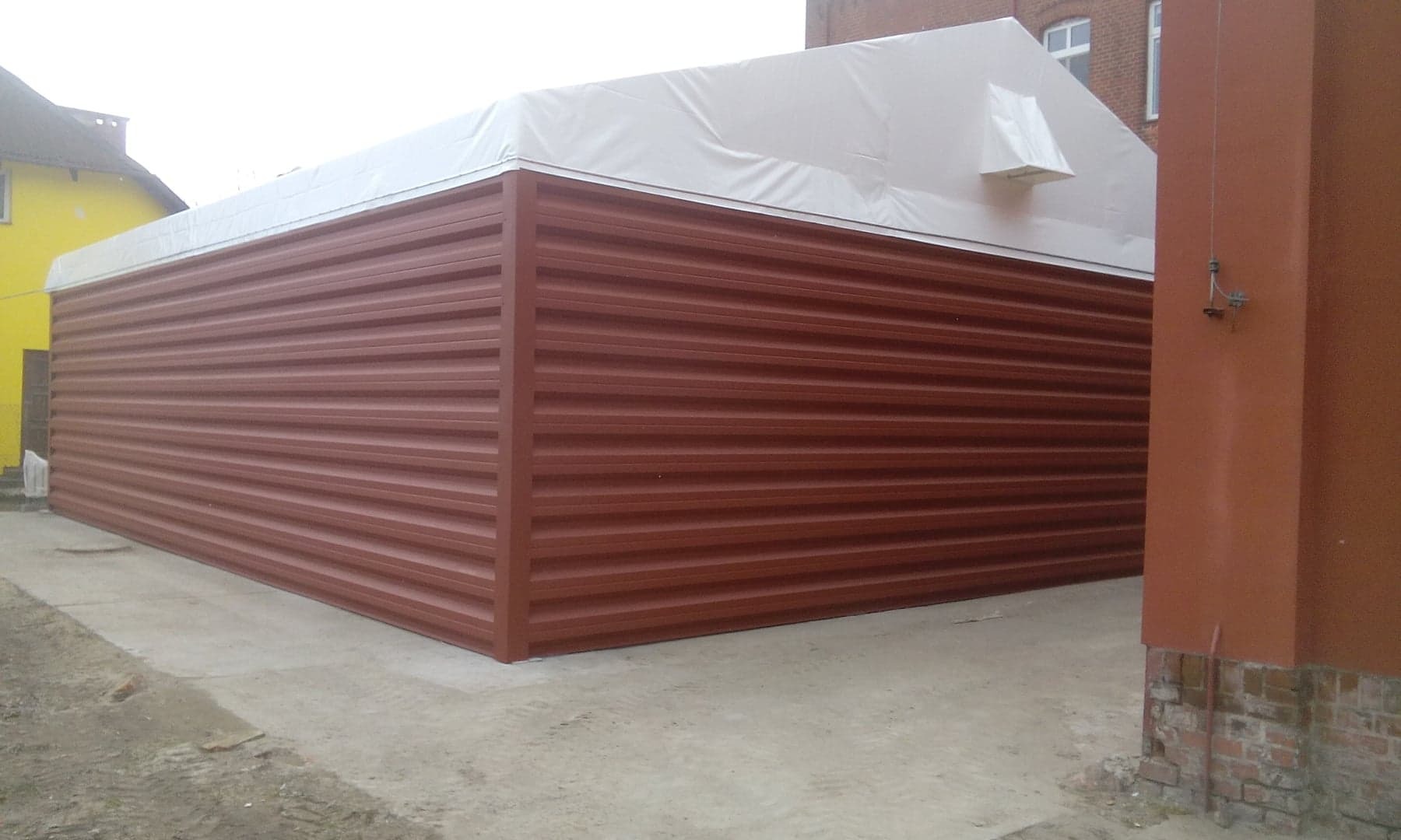 Gotowa konstrukcja hali z brązowych płyt warstwowych z białym dachem na betonowej posadzce, widok z zewnątrz.