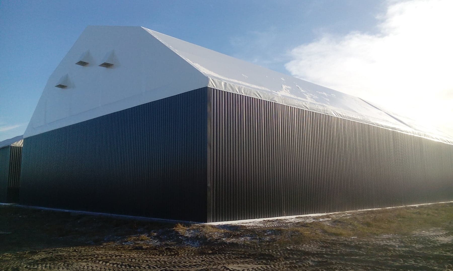 Duża hala magazynowa z szarej blachy trapezowej i białego dachu membranowego, widok z zewnątrz w słoneczny dzień.
