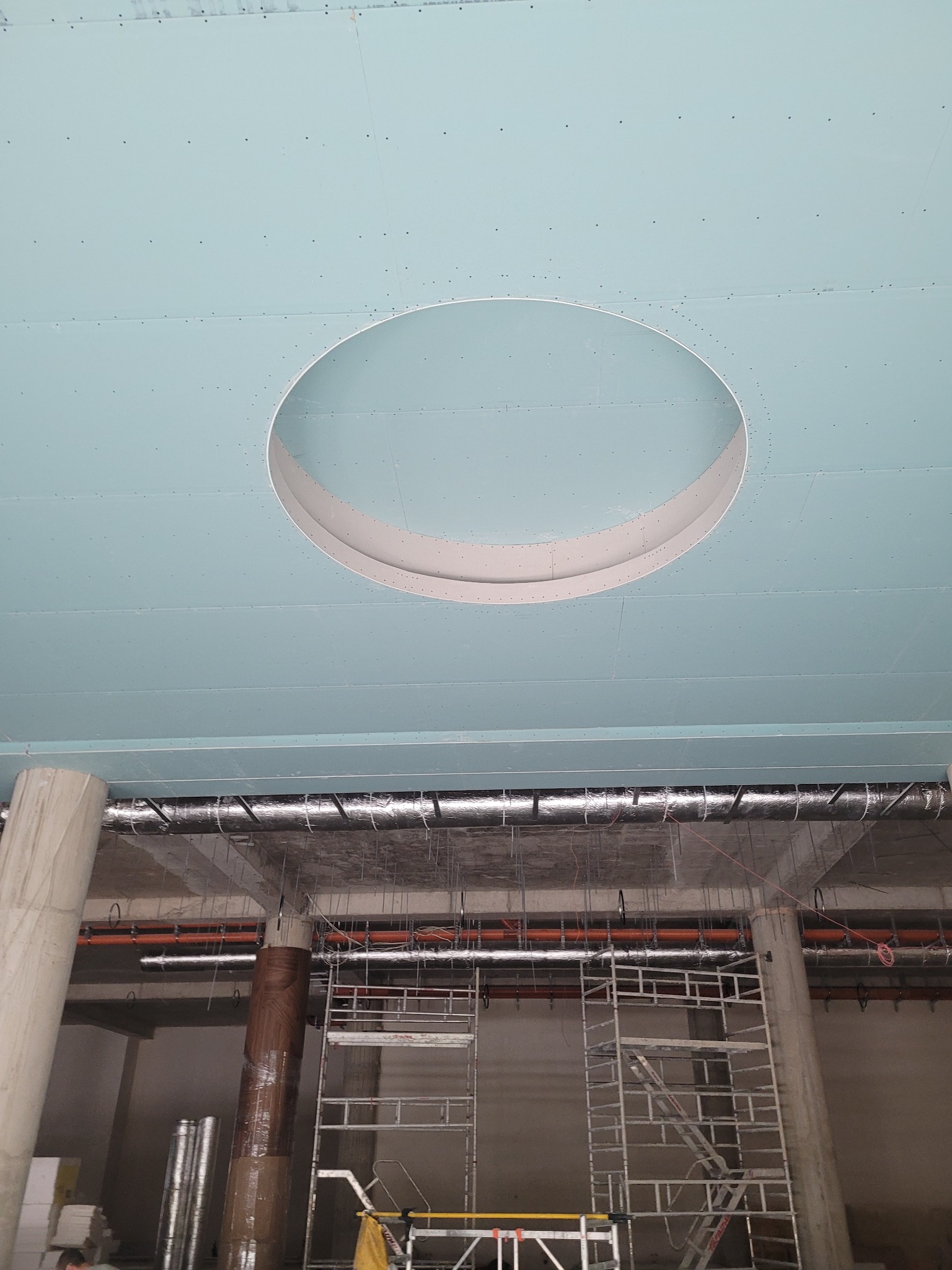 Montaż sufitu podwieszanego z otworem na oświetlenie. Widoczne płyty, rusztowanie i instalacje. Prace wykończeniowe w nowym budynku.