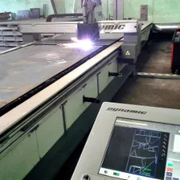 Proces cięcia plazmowego grubej blachy stalowej na stole CNC z widocznym panelem sterowania i iskrami podczas pracy.