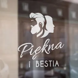 Biały napis 'Piękna i Bestia' oraz grafika przedstawiająca profile kobiety i mężczyzny umieszczone na szklanej witrynie salonu.