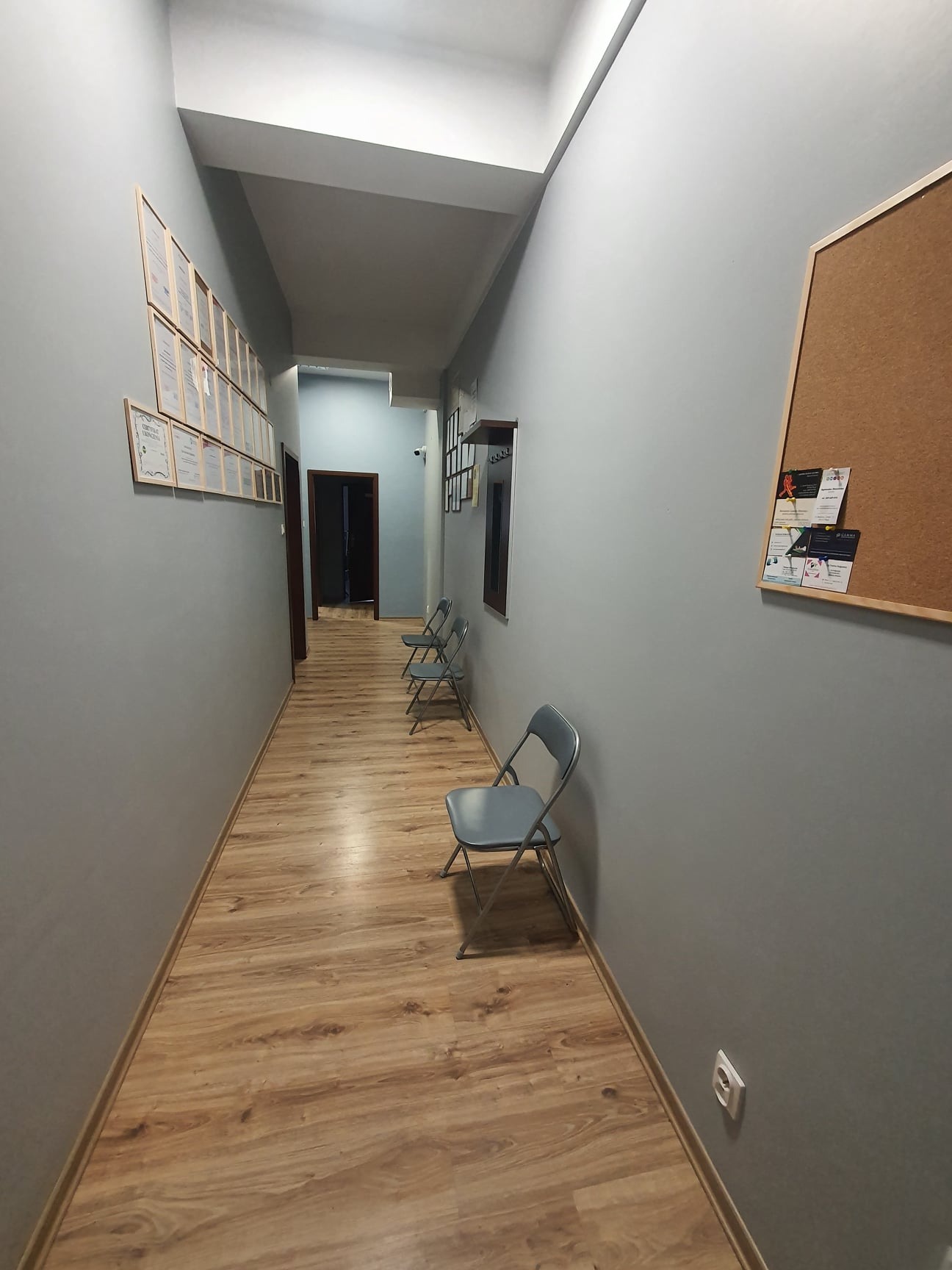 Korytarz poczekalni gabinetu logopedycznego w Płocku z krzesłami dla pacjentów, dyplomami na ścianie i tablicą korkową.