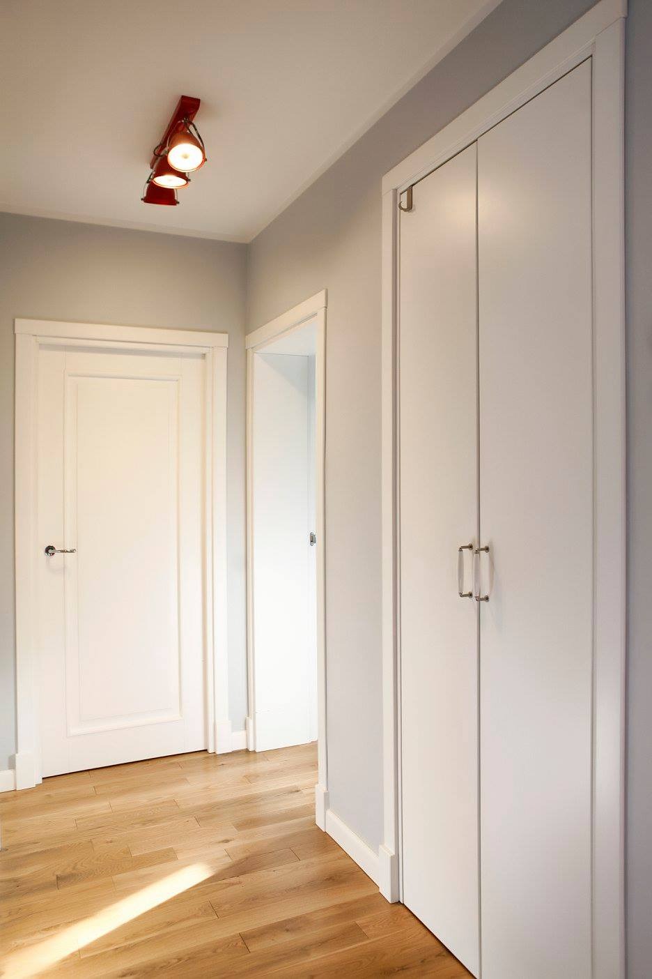 Korytarz w odcieniach szarości z drewnianą podłogą, oświetleniem punktowym i białymi drzwiami oraz szafą z podwójnymi drzwiami i metalowymi uchwytami.