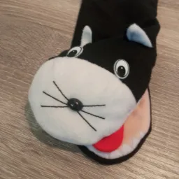 Czarno-biała pacynka w kształcie kota z wystającą czerwoną częścią imitującą język, leżąca na drewnianej powierzchni.