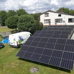 Ekotechnika OZE - Panel słoneczny na dachu domu jednorodzinnego, obok zaparkowany samochód i bus z logo firmy, w tle drzewa i błękitny basen.