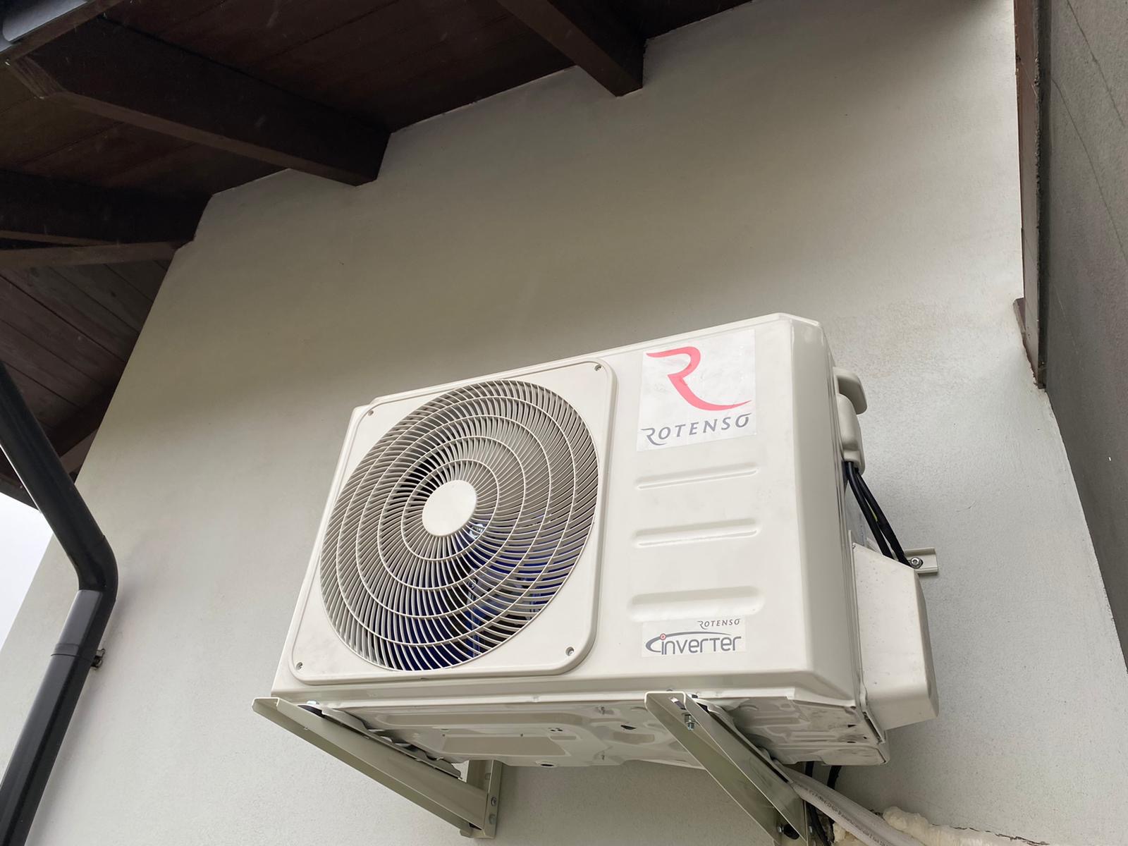 Zamontowana jednostka zewnętrzna klimatyzacji Rotenso Inverter na szarej ścianie budynku, widoczny fragment dachu i rynna.