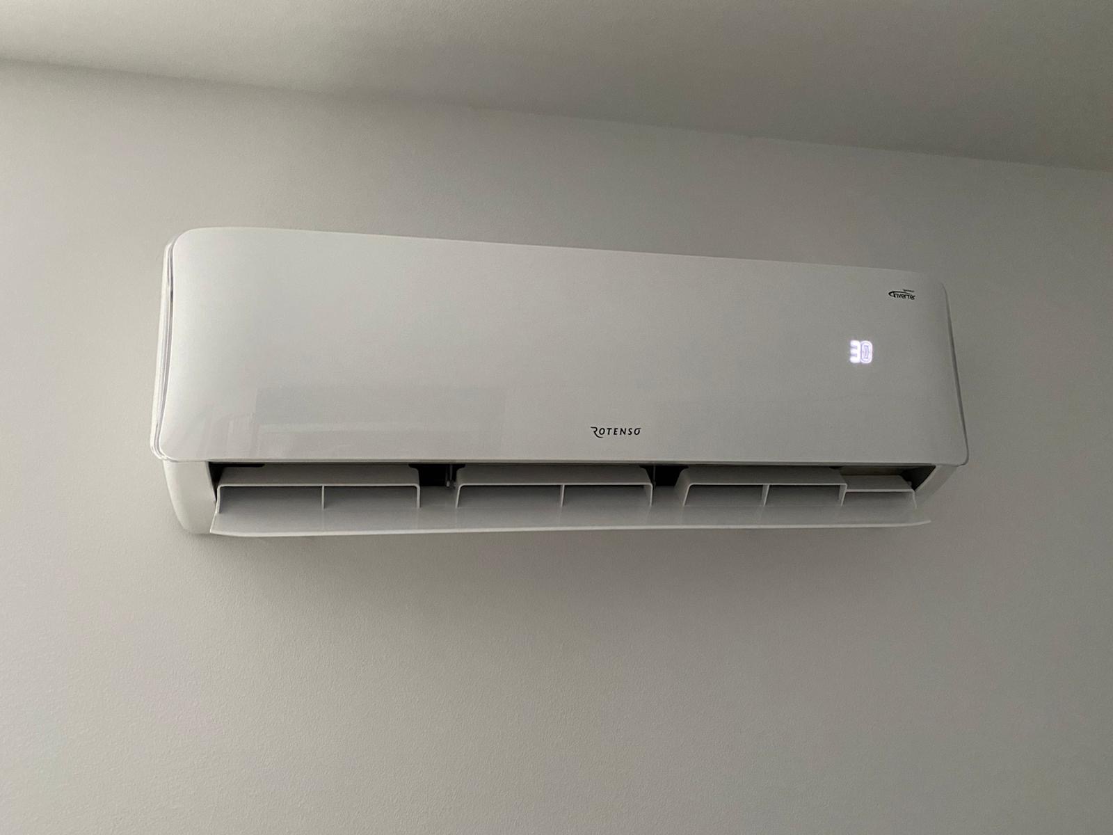 Biała jednostka klimatyzacji Rotenso zamontowana na jasnoszarej ścianie, wyświetlająca temperaturę 30 stopni Celsjusza.