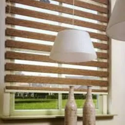 Roleta dzień noc z brązowymi pasami na oknie, widoczne dwie ceramiczne butelki na parapecie i lampa wisząca.