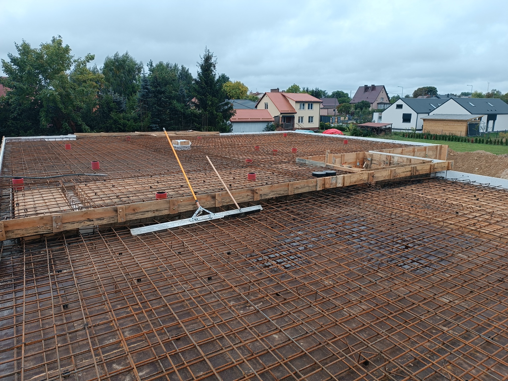 Zbrojenie płyty fundamentowej z deskowaniem na budowie domu w Szczytnie, widoczne narzędzia i elementy instalacji.