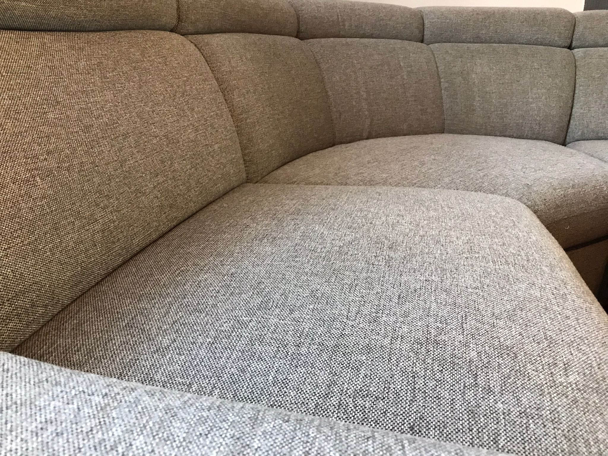 Fragment narożnika z szarej, teksturowanej tkaniny, z widocznymi przeszyciami i zaokrąglonymi kształtami.