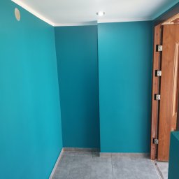 FIRMA BUDOWLANA ROMAN KOVALYK - Turkusowe ściany, szara podłoga i biały sufit z oświetleniem punktowym. Widoczne drzwi z brązową ościeżnicą. Świeżo pomalowane wnętrze po remoncie.
