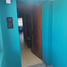 FIRMA BUDOWLANA ROMAN KOVALYK - Turkusowe ściany po malowaniu w korytarzu z otwartymi drzwiami. Widoczne detale wykończenia i płytki podłogowe w dwóch odcieniach.